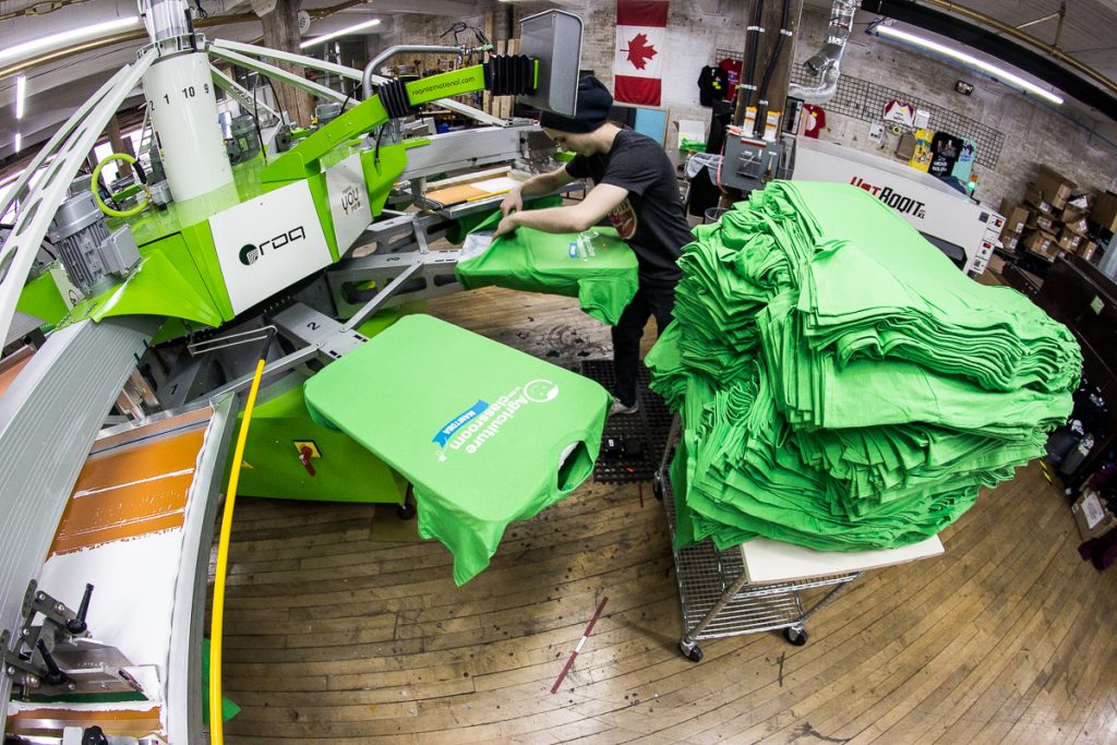 Press operator running a job of green tees on the automatic press at Floodway in Winnipeg