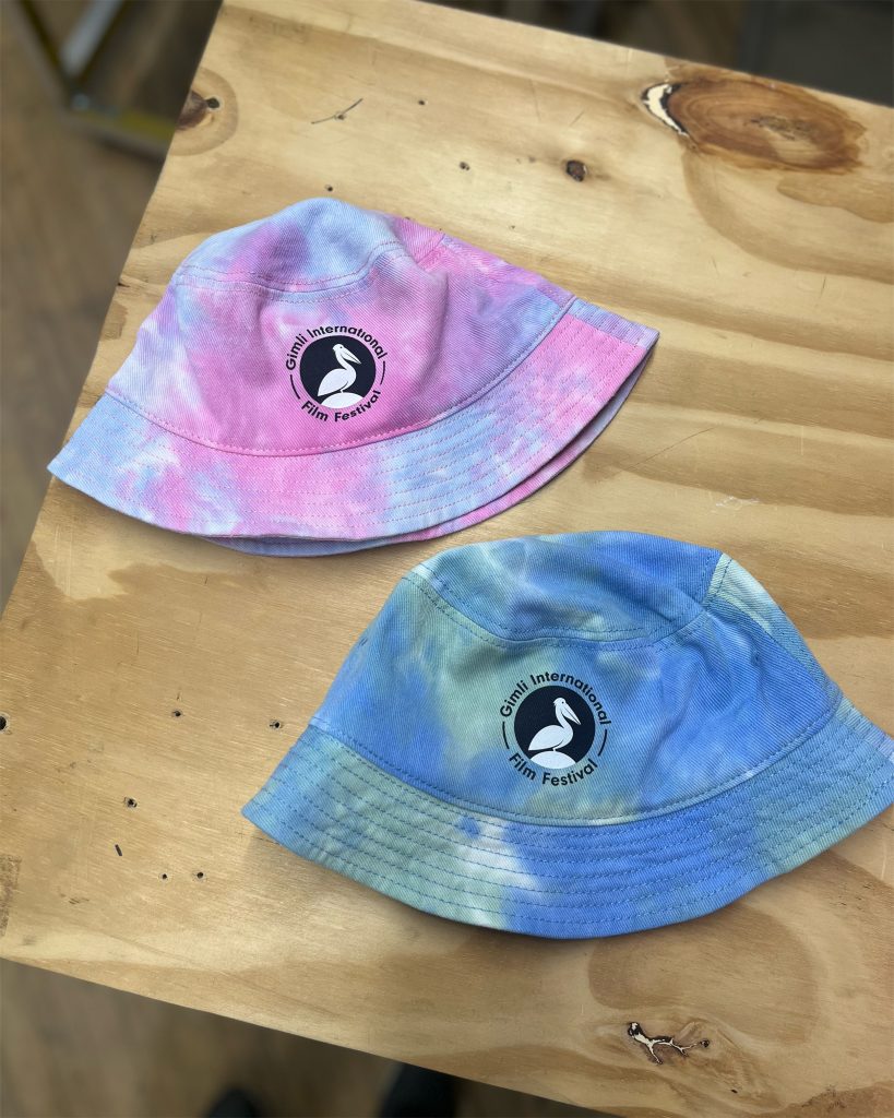 Two tie dye bucket hats printed with the Gimli International Film Festival logo, on a workbench