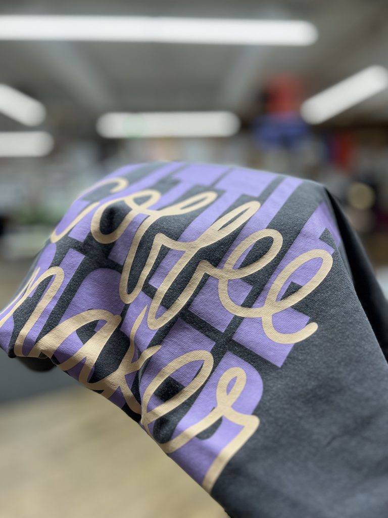 Close-up of a charcoal tee with a two colour script print in cream over purple