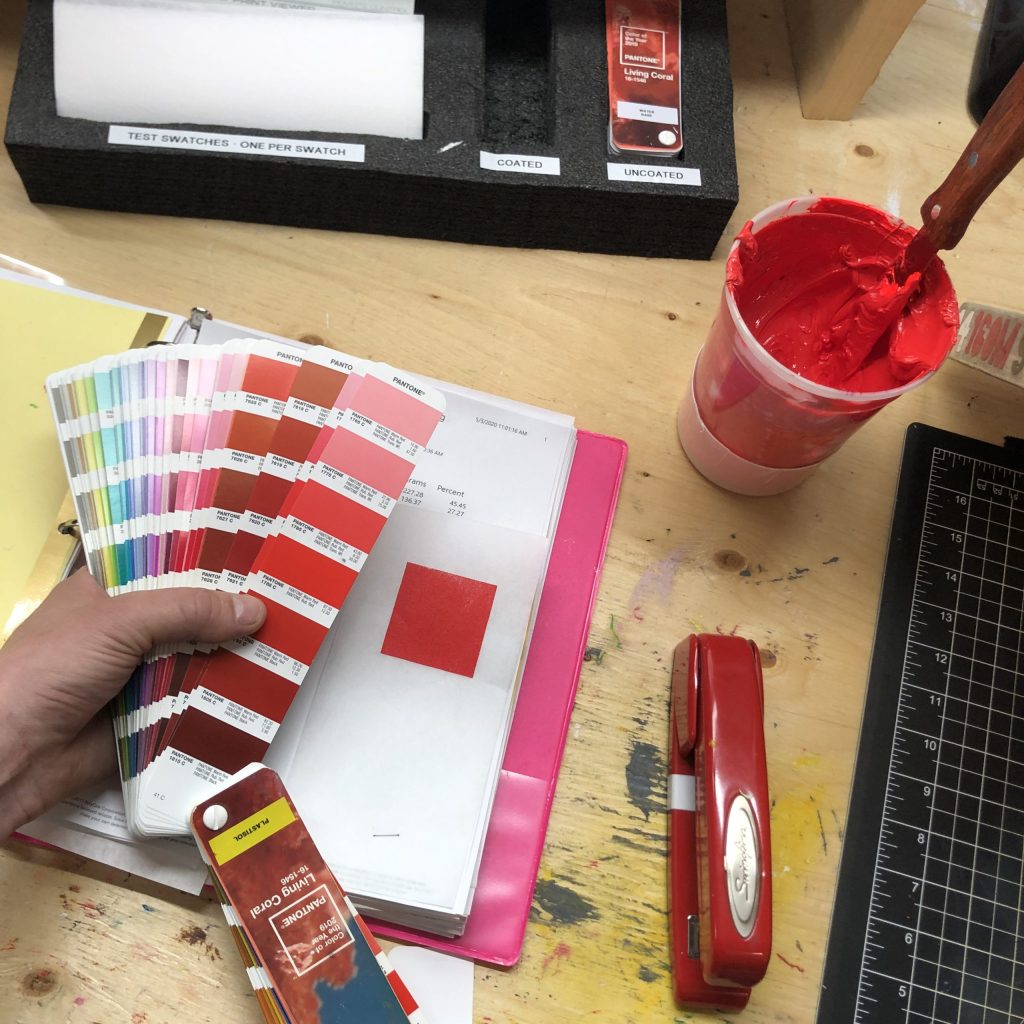 A hand fanning open a Pantone swatch book beside a tub of red ink on the shop's colour matching bench