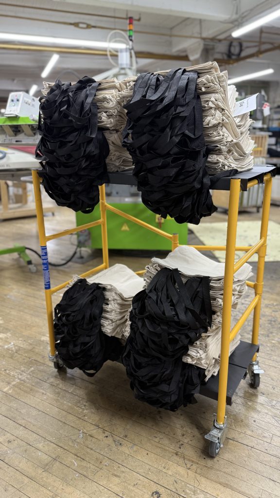 A rolling cart stacked with folded black and natural tote bags on the shop floor