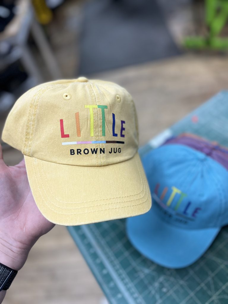 Yellow cap with a multicolour Little Brown Jug logo, a blue one sitting behind it