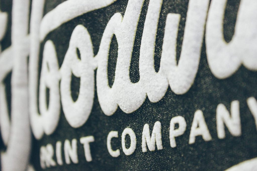 Close up of the white Floodway Print Company script lettering printed on a dark textured garment