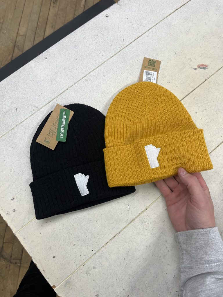 Black and gold ribbed beanies with a white embroidered Manitoba shape on the cuff, hang tags still attached