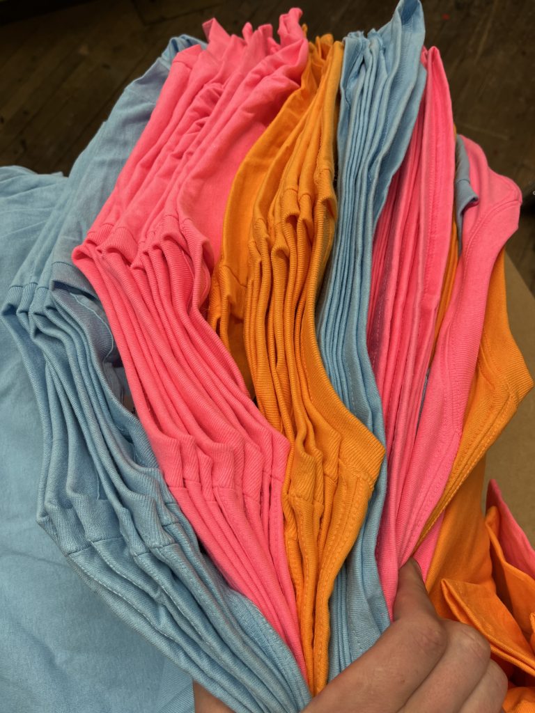 Stacks of blank tees fanned out in light blue, pink and orange