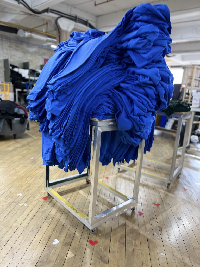 A large pile of royal blue tees heaped on a steel rolling cart on the shop's wood floor