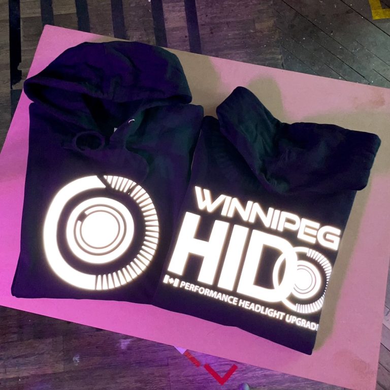 Two black hoodies with reflective Winnipeg HID prints lighting up under the camera flash